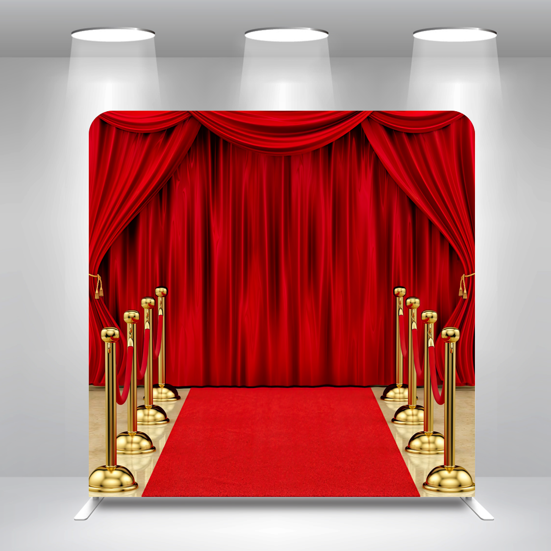 Red velvet stage with closed curtain, red carpet, and gold stanchions with red ropes overhead, lit by ceiling spotlights.