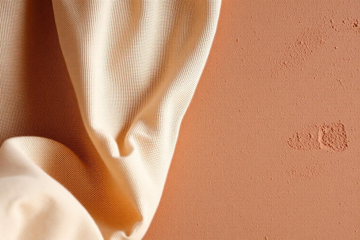 Close-up of a beige fabric draped over a textured peach-colored surface with small irregularities.