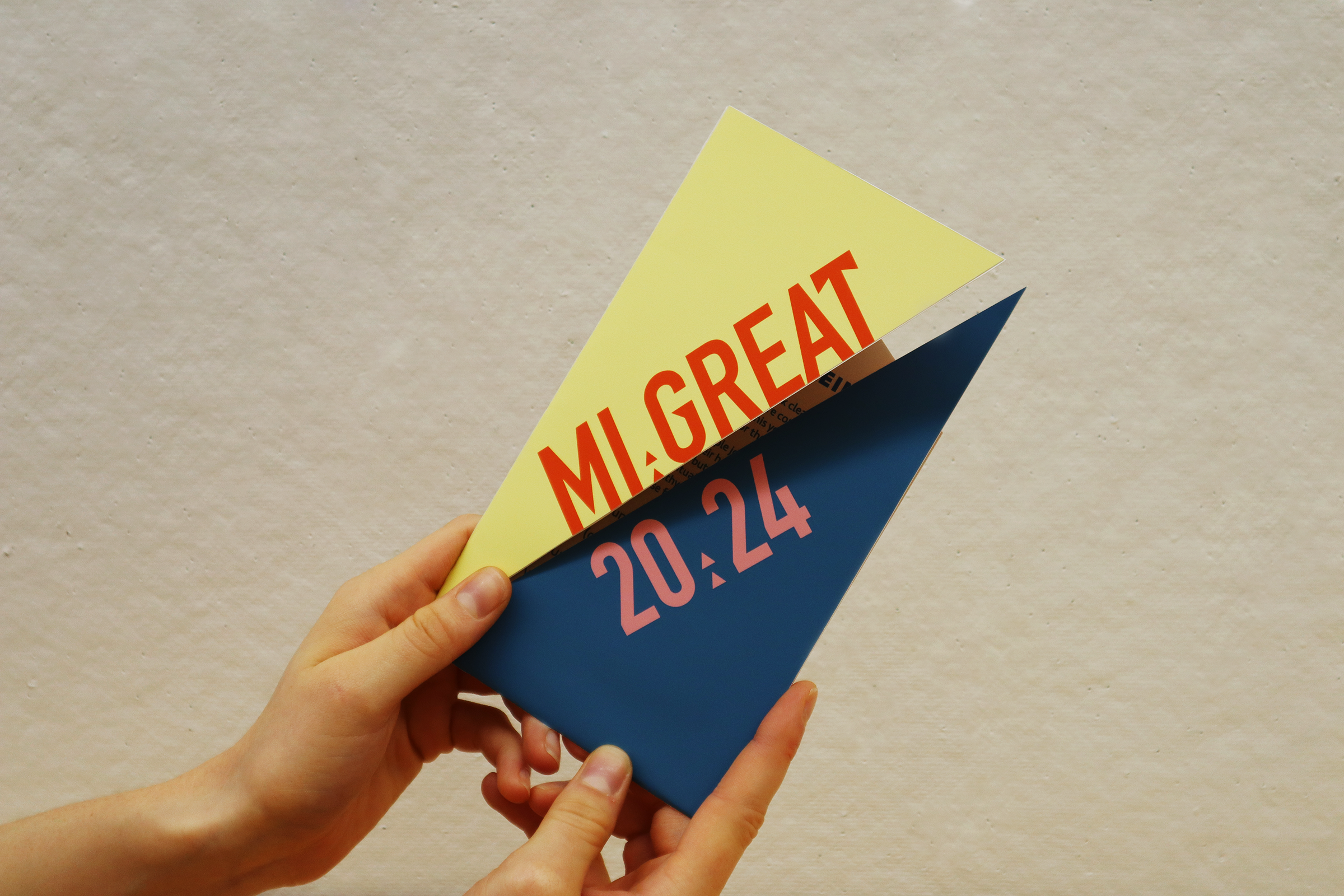 Close-up of a hand holding colorful flyers with event information against a beige wall.