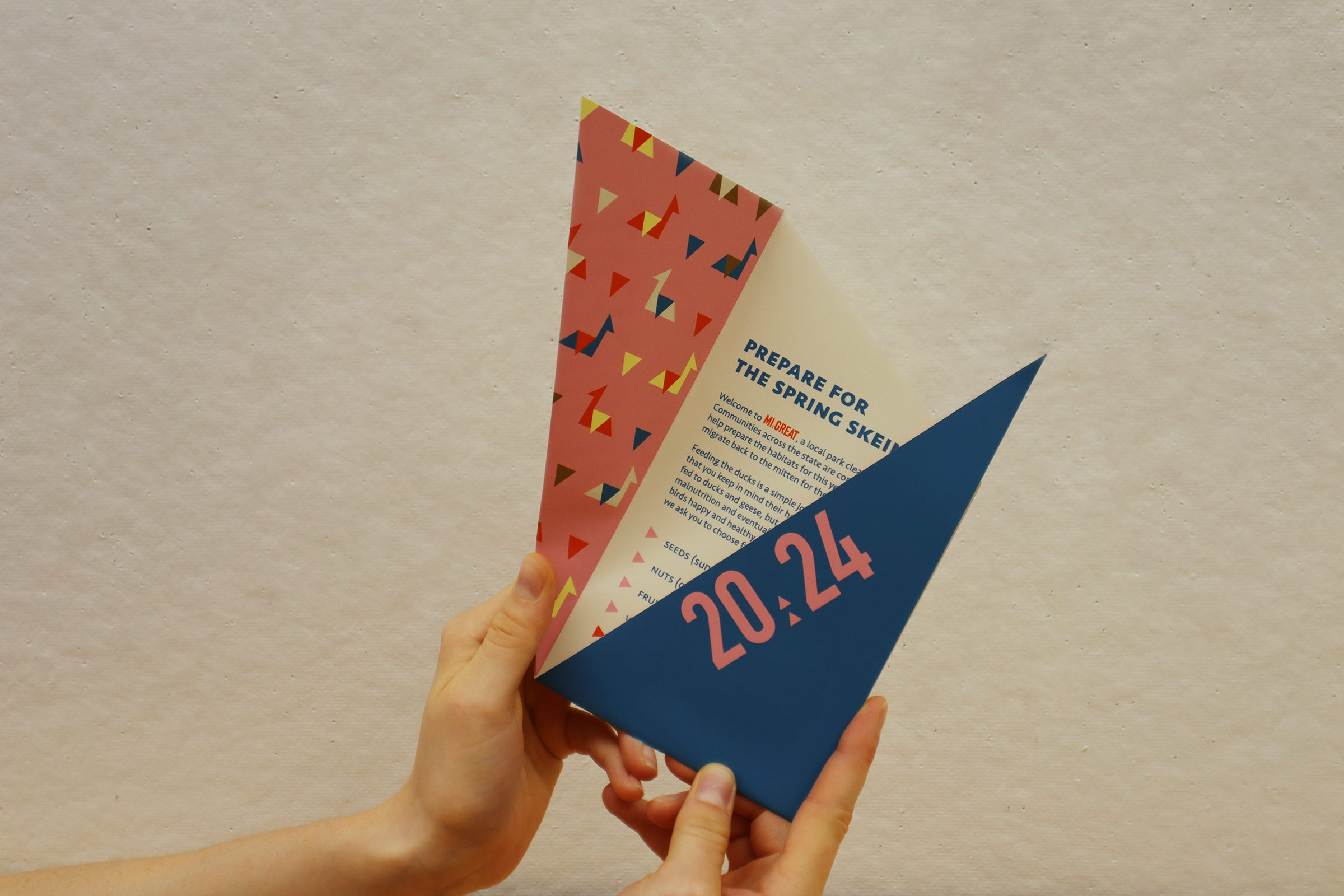 Close-up of a hand holding a colorful event flyer with the date 2024 on it against a beige wall.