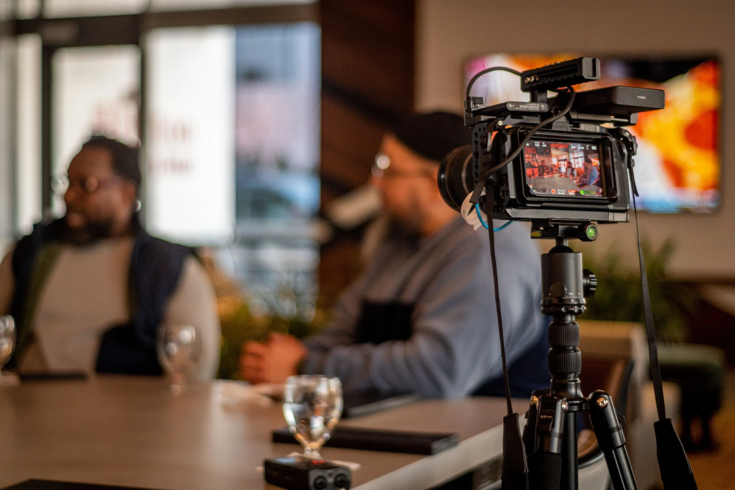 A professional video camera on tripod recording a meeting in a modern conference room.