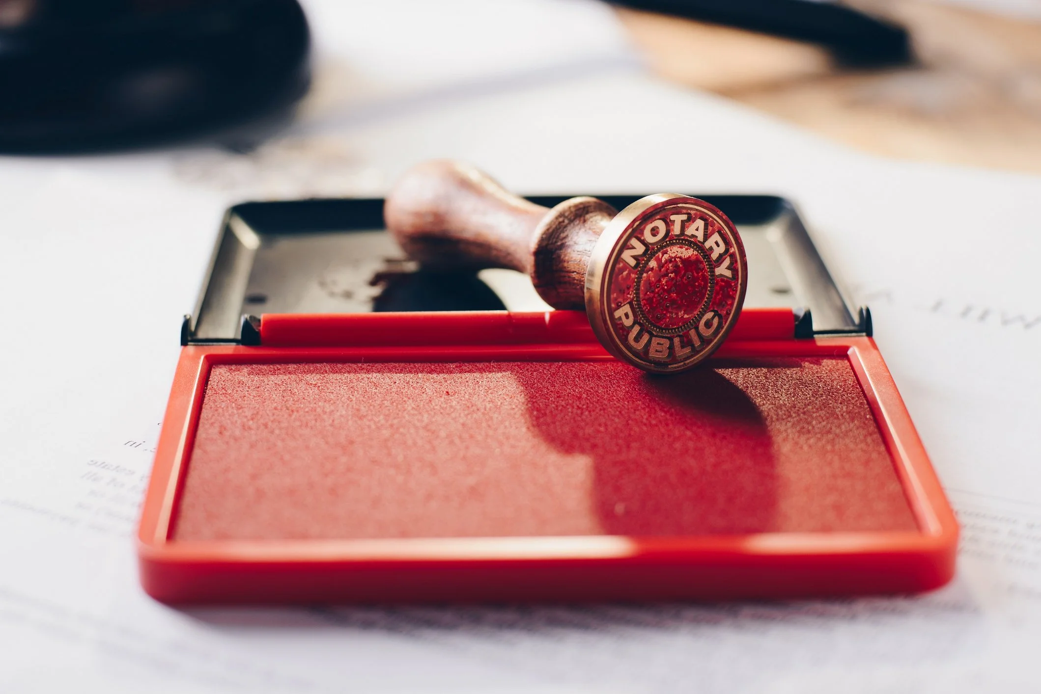 A rubber stamp with the words 'Notary Public' in red ink resting on a red pad, placed on a white surface with printed documents underneath.