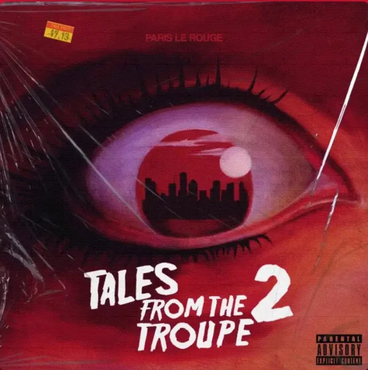 Red album cover with an illustration of an eye containing a city skyline reflected in the iris. Text reads "Tales from the Troupe 2" and includes a parental advisory label.