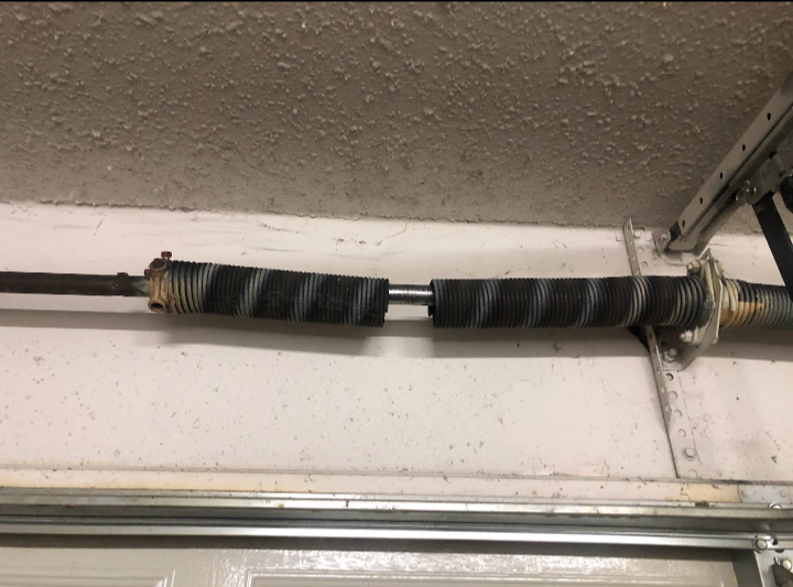 Garage door torsion spring system with worn and aged components mounted above a garage door opening.