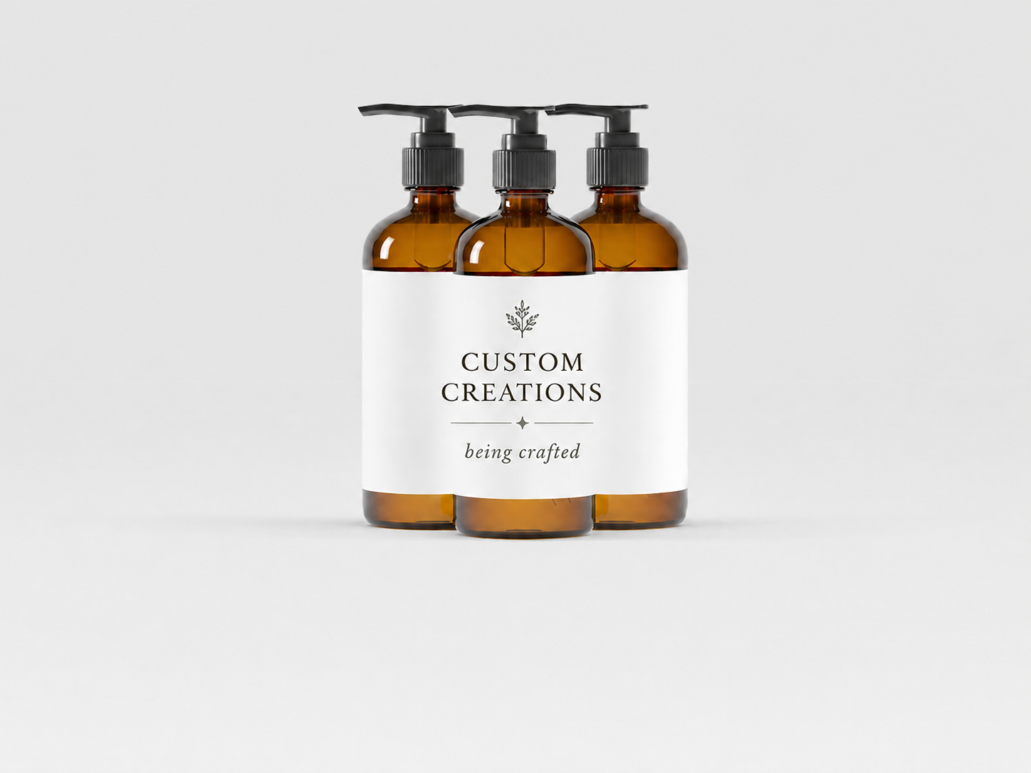Three amber glass bottles with black pump dispensers, labeled "Custom Creations" with the tagline "being crafted" on a white background.