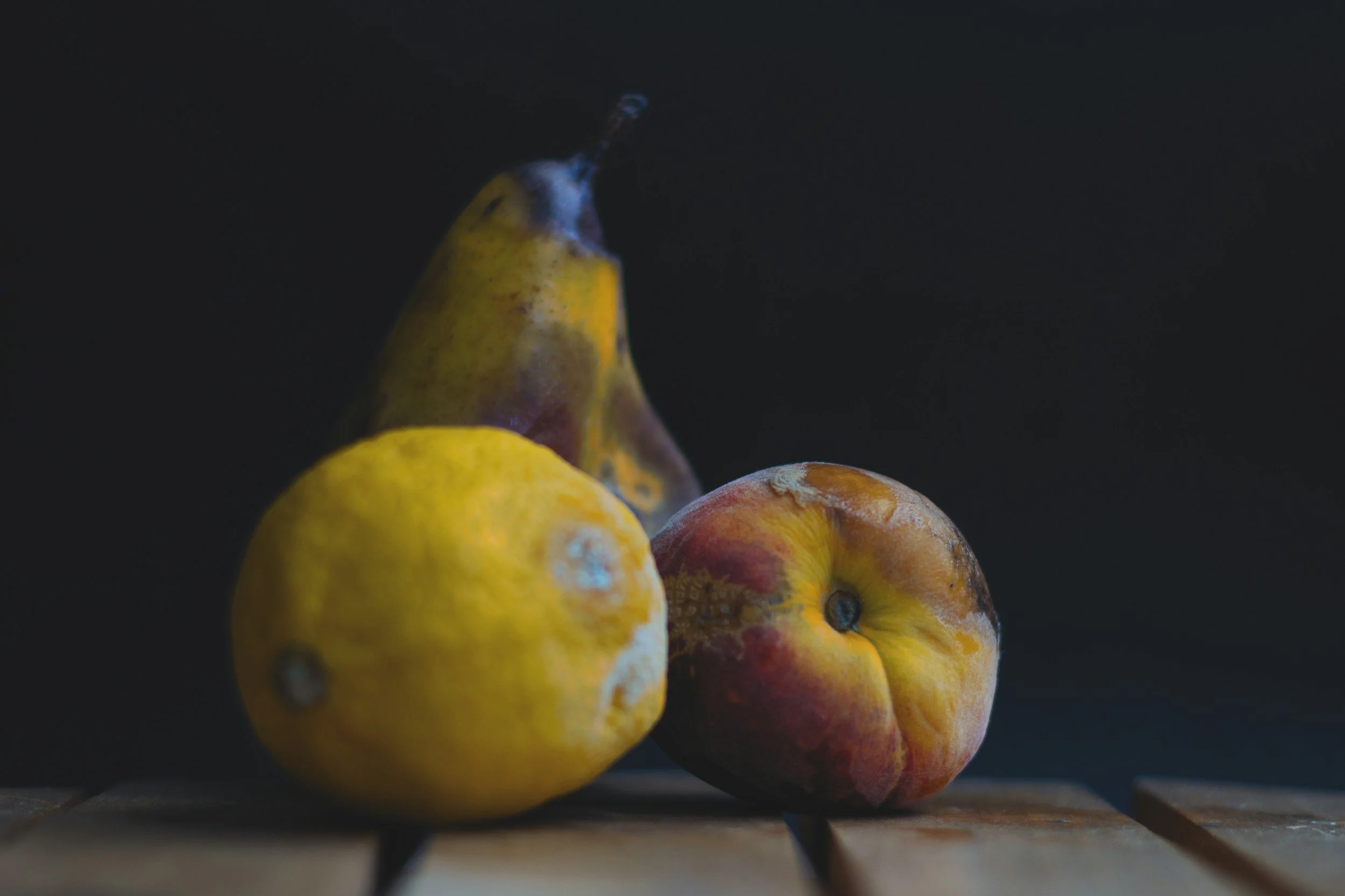 Close-up of several ripening pears with yellow, green, and reddish hues against a dark background.