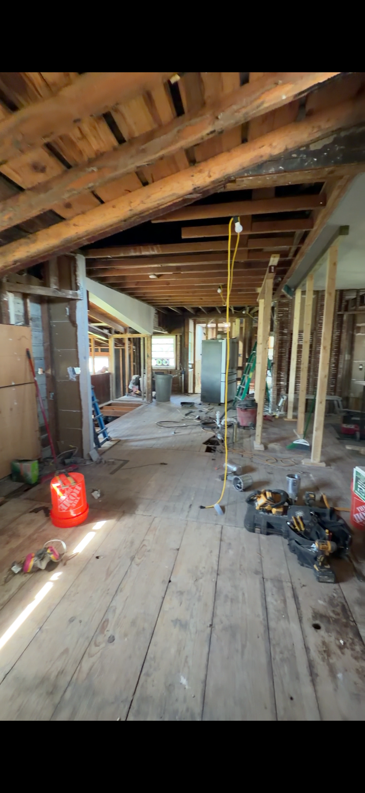 Interior view of a room under construction with exposed wooden beams, construction tools, and scattered construction materials and debris.