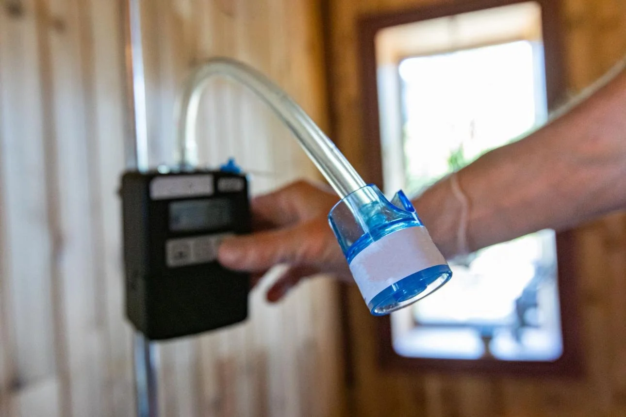 Close-up of a person holding a transparent tube connected to a medical device in a room with wooden walls and a window in the background.