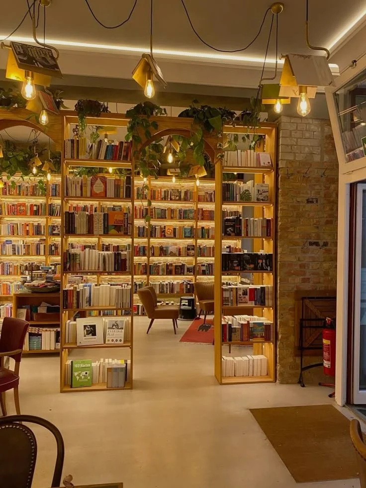 Cozy bookstore with wooden bookshelves filled with books, warm lighting from hanging bulbs, and comfortable chairs for reading.