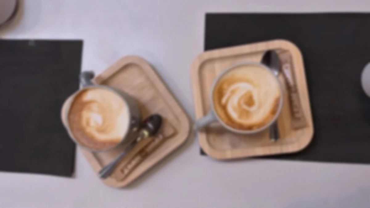 Two cups of coffee with latte art on wooden trays, with spoons and chocolate bars on black napkins on a table.