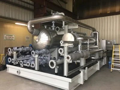Industrial machinery with pipes, valves, and a large cylindrical tank inside a warehouse