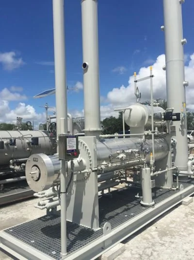 Industrial natural gas compressor installed outdoors with pipes and control panel, under partly cloudy sky.