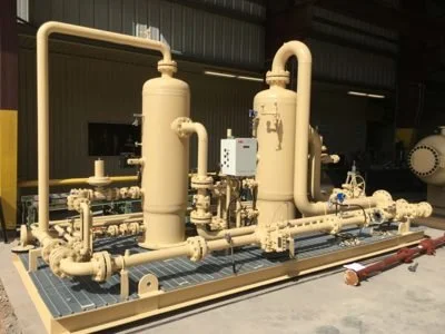 Industrial equipment with large beige pipes and valves mounted on a platform in a warehouse or factory setting.