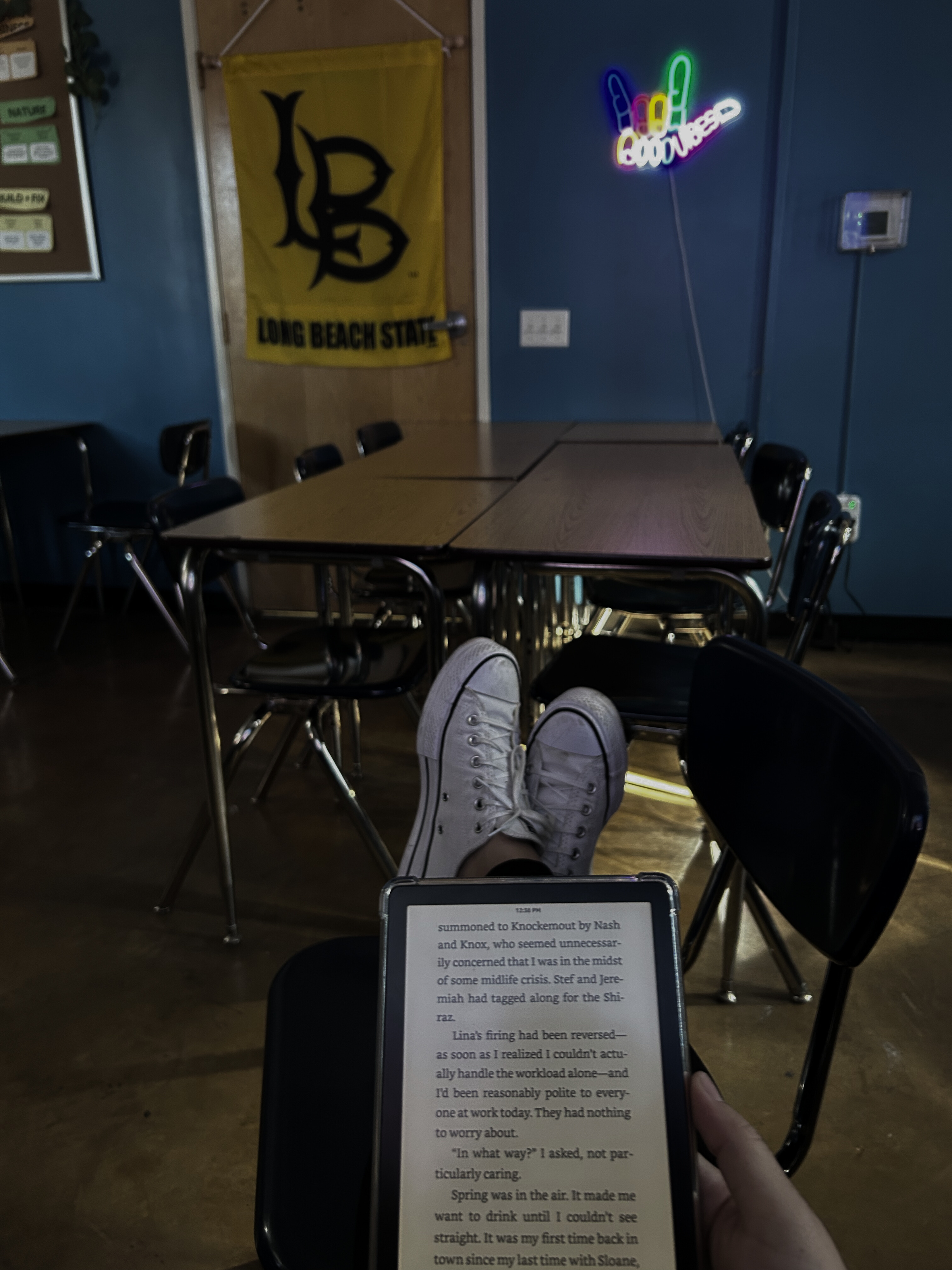 The image shows a teacher in her classroom, the room has soft lighting, fun decor with a neon sign on the wall
