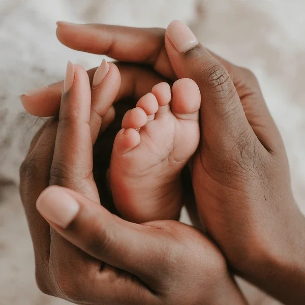 Close-up of a tiny baby foot being gently held by two hands with dark and light skin tones.