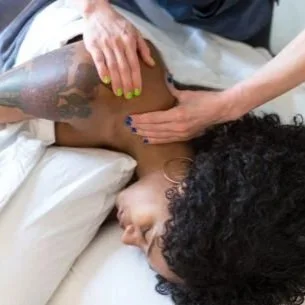 A person receiving a massage on their upper back and shoulder area in a clinical or spa setting.