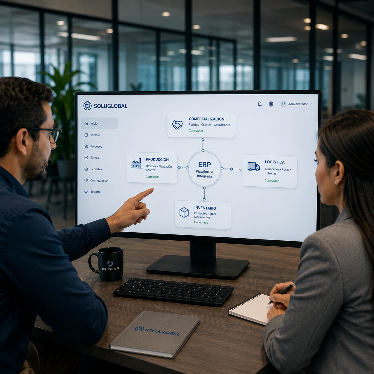 Dos personas en una oficina revisando un diagrama de sistema ERP en una pantalla, con notas y objetos de oficina en la mesa.
