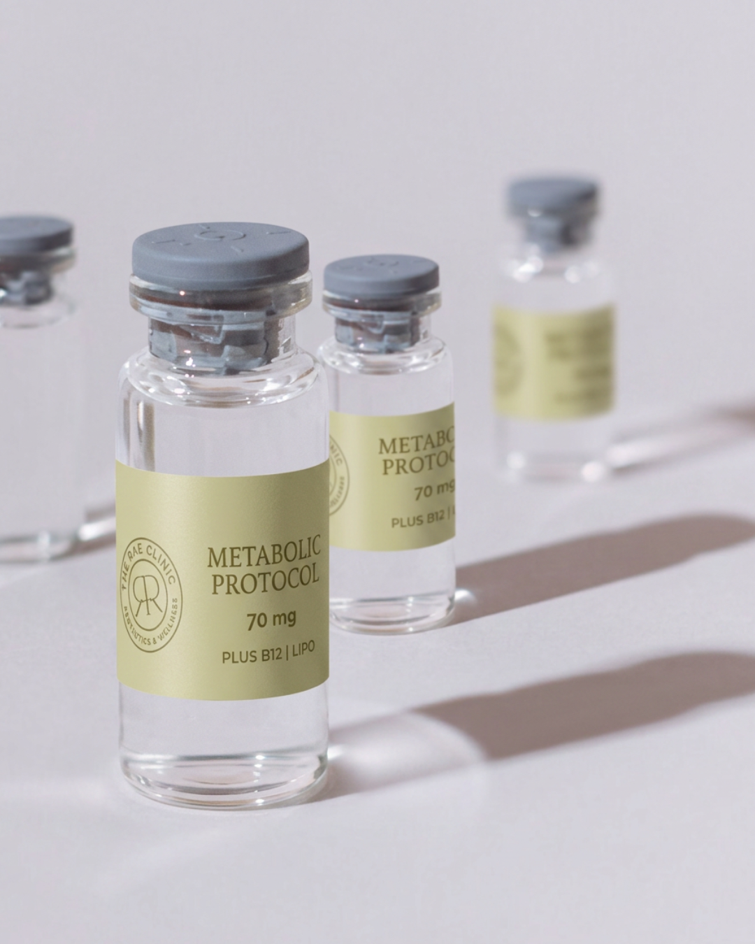 Three small glass vials labeled "Metabolic Protocol 70 mg" with gray caps are on a white surface, casting shadows.