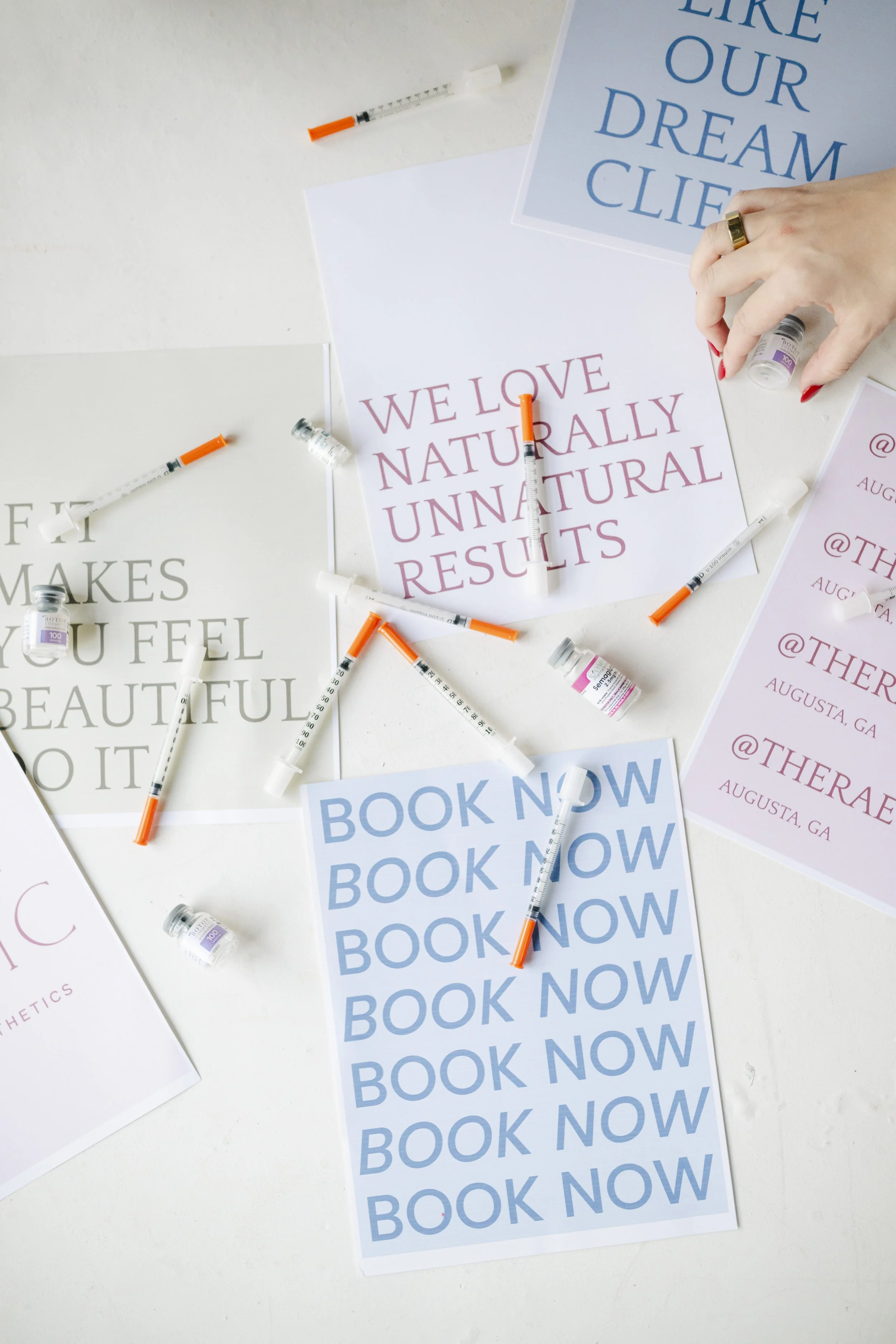 Multiple motivational posters on a white surface, with syringes and small vials of medication scattered around. One poster reads 'WE LOVE NATURALLY UNNATURAL RESULTS' and another 'LIKE OUR DREAM LIFE'.