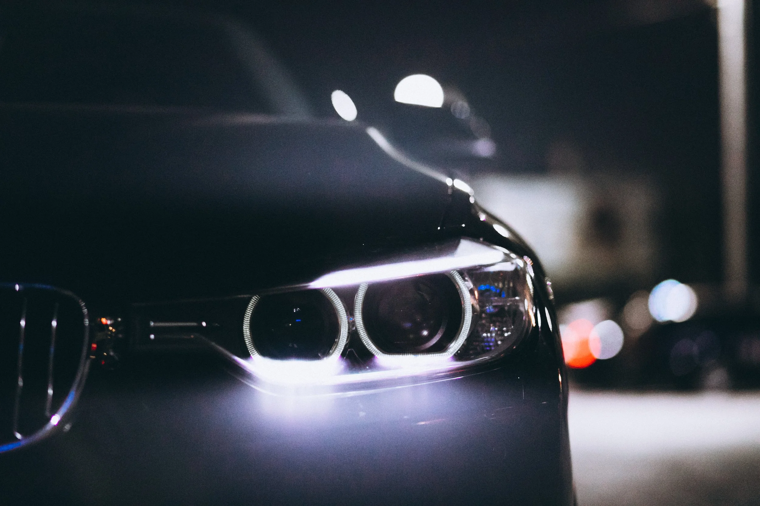 Close-up of a car's front headlight with a dark background and bokeh lights.