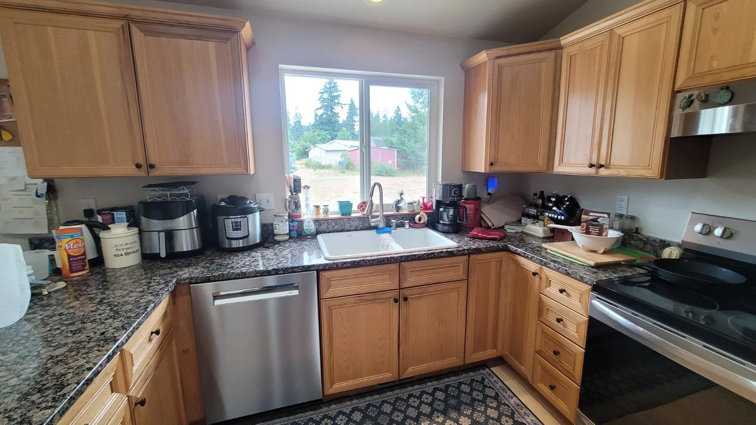 Well-equipped kitchen with wood cabinets, granite countertops, double sink, stainless-steel dishwasher, electric range, coffee maker, and small appliances.