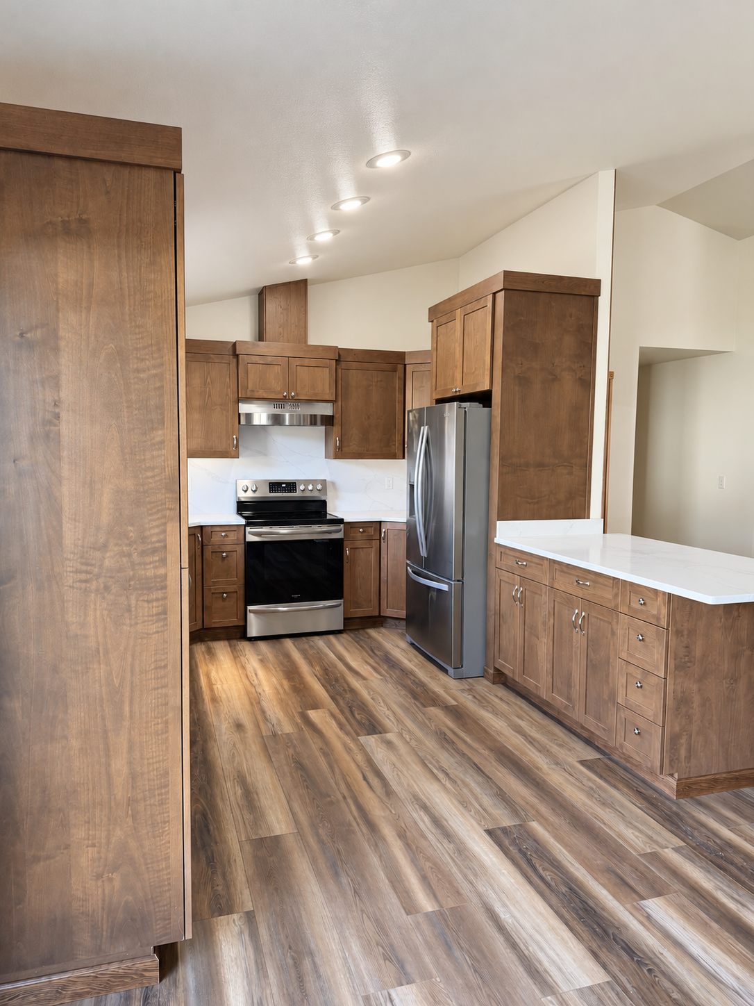 Modern kitchen with dark wood cabinets, stainless steel appliances, white countertops, recessed lighting, and wood-look flooring