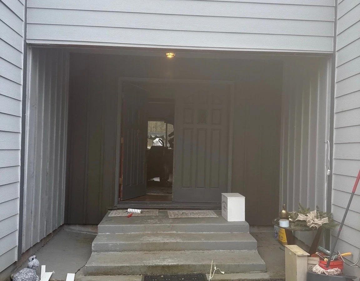 Open garage entry with concrete steps, double doors, doormat, potted plants, and cleaning supplies