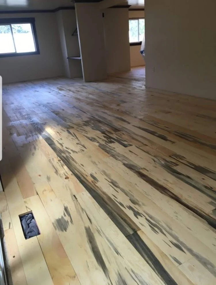 Room with partially installed wood flooring and two large windows with view outside.