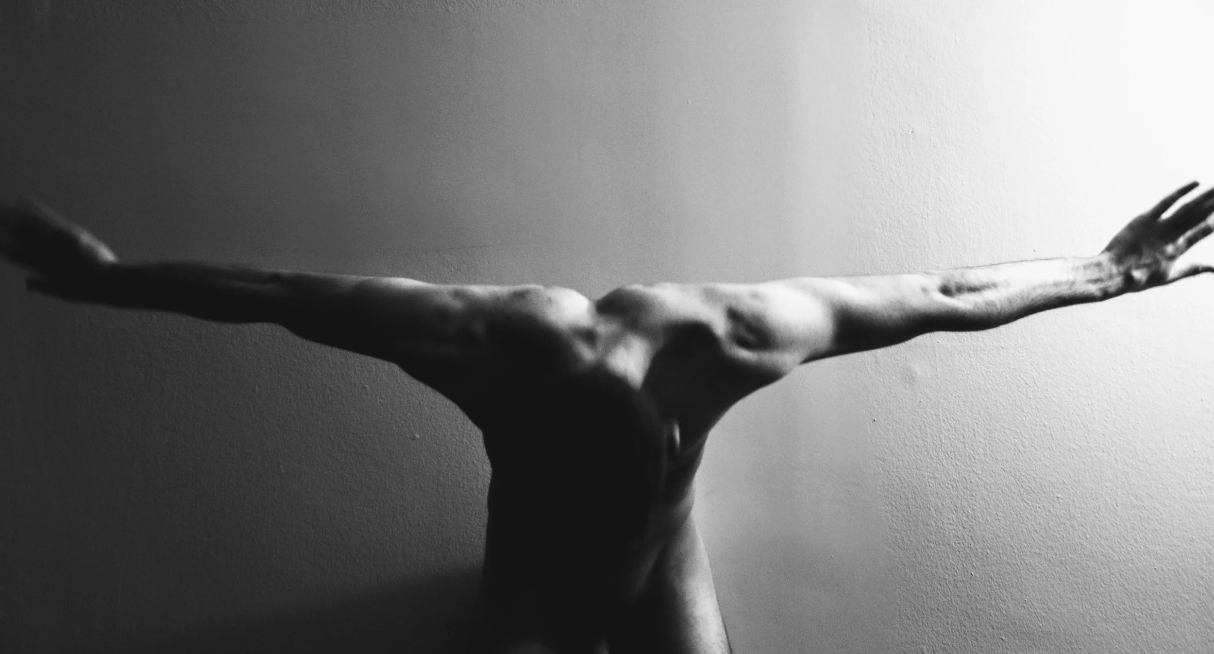 A black-and-white photograph of a human hand with fingers extended, viewed against a plain wall.