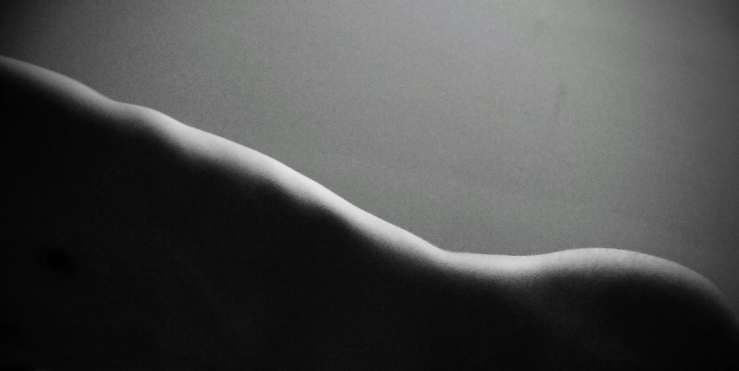 Close-up of a smooth, curved, matte surface with dramatic lighting creating shadows and highlights.