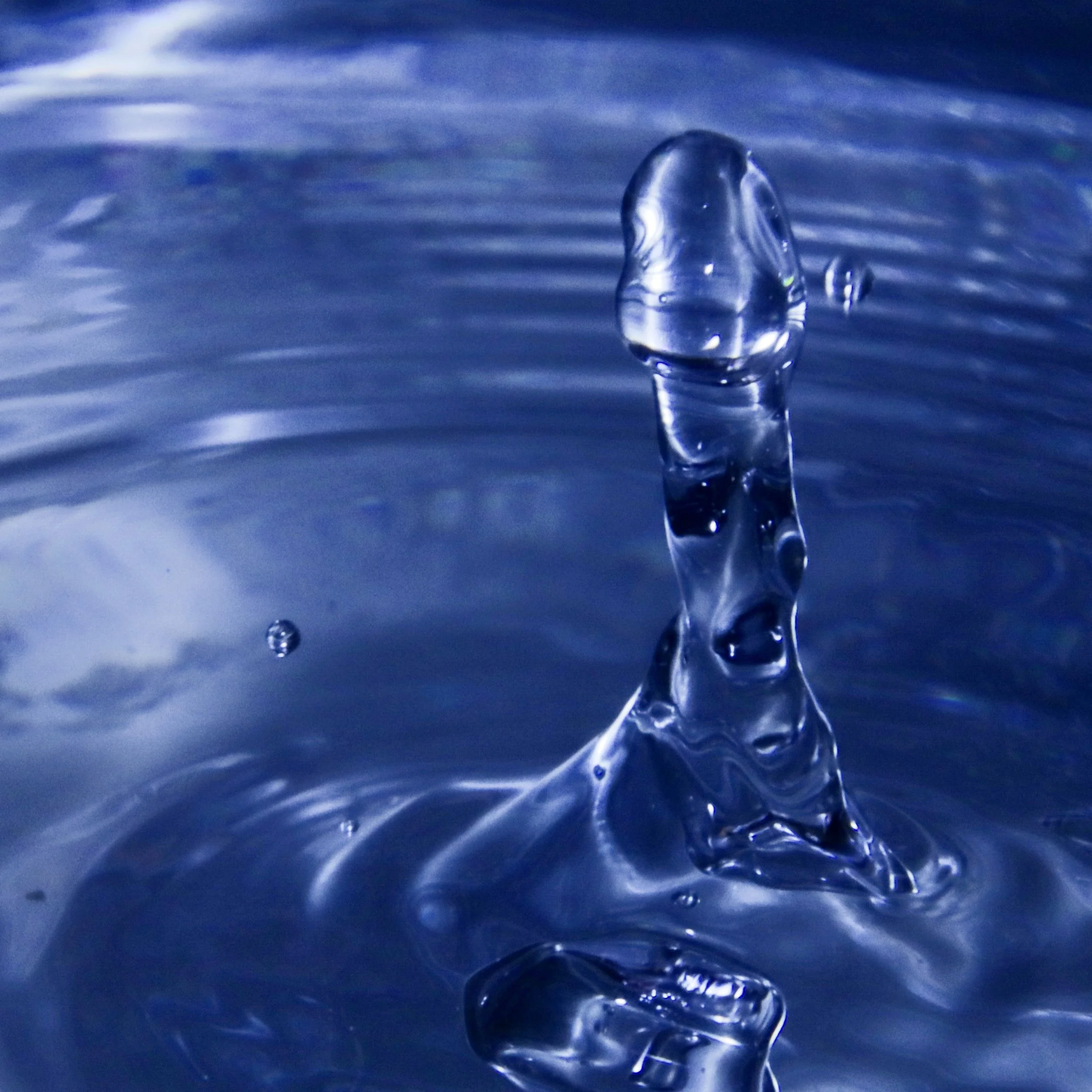 Close-up of a water droplet splashing into a blue liquid surface.