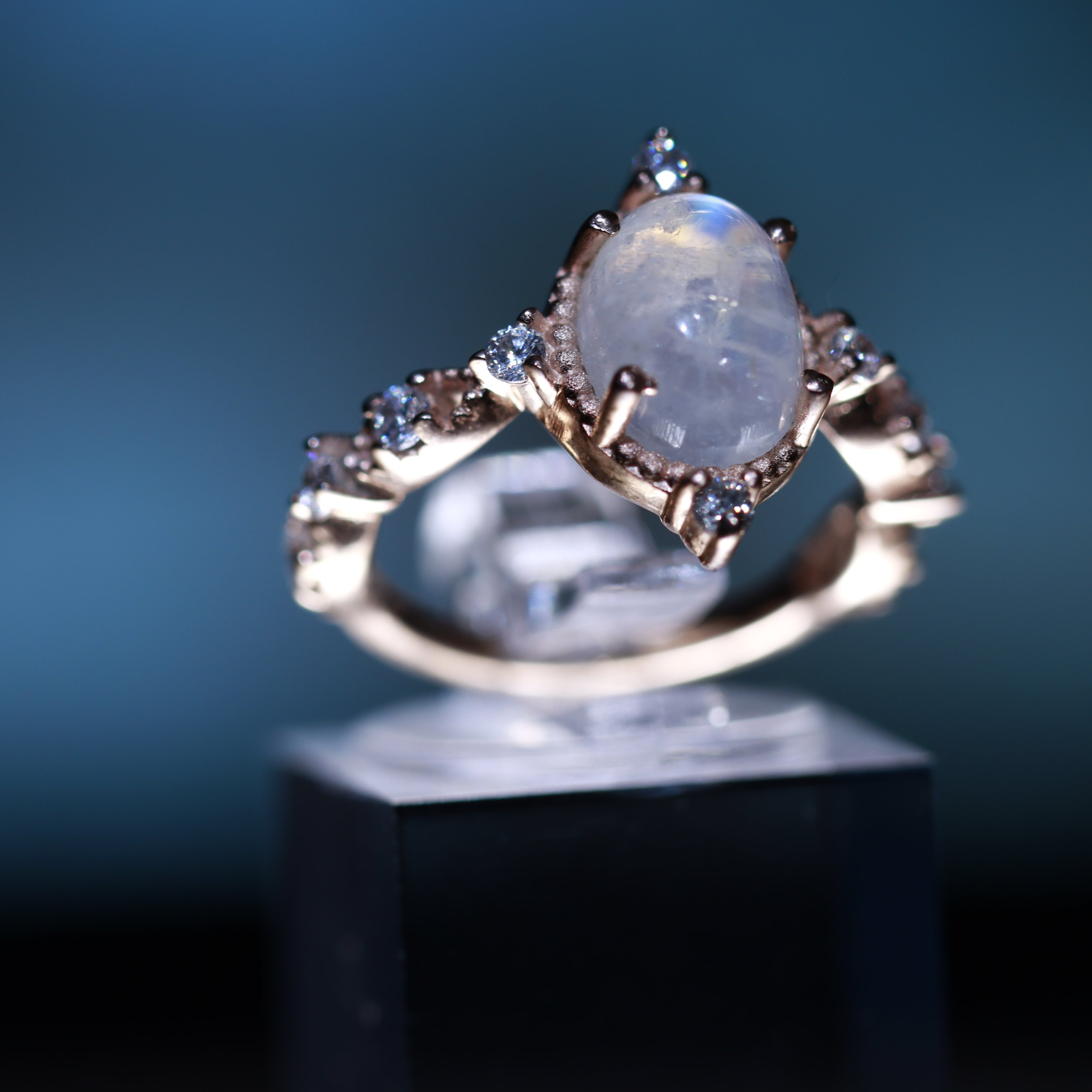 Close-up of a ring featuring a large oval-shaped opal gemstone and small diamonds set in a metal band against a dark background.