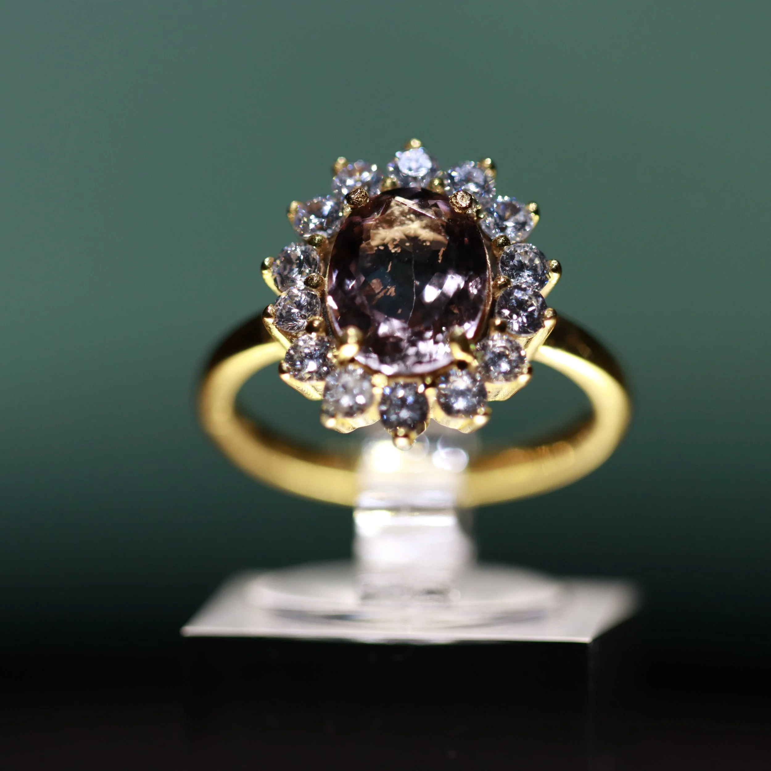 Close-up view of a gold ring with a large central purple gemstone surrounded by small white diamonds, displayed on a reflective surface.