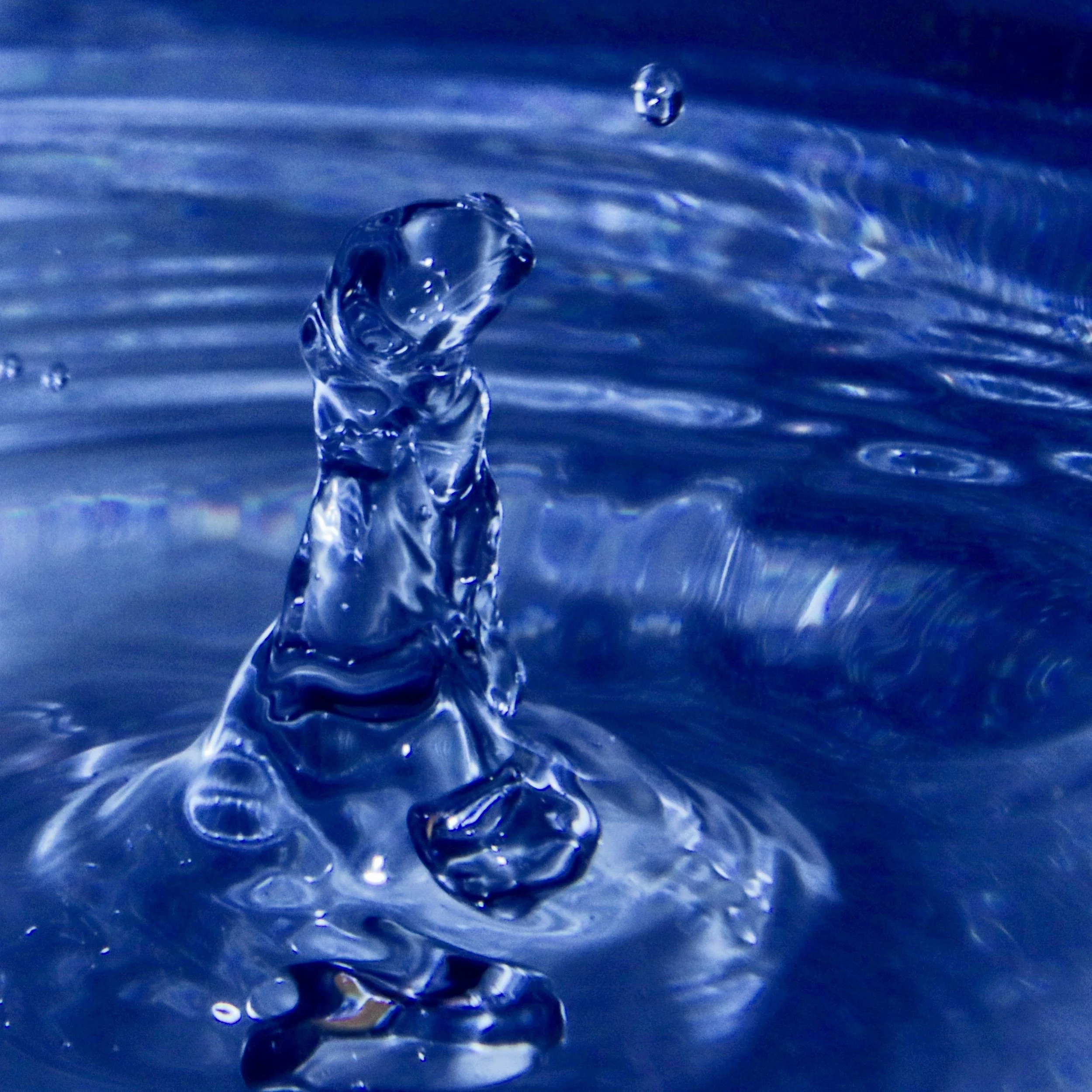 Close-up of clear water droplets causing ripples on a blue water surface.