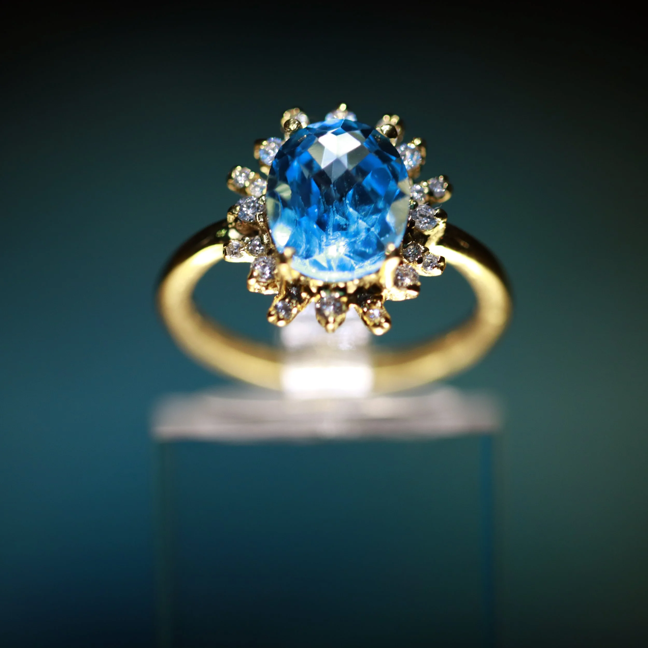 Close-up of a gold ring with a large blue gemstone surrounded by small diamonds, showcasing intricate jewelry design.