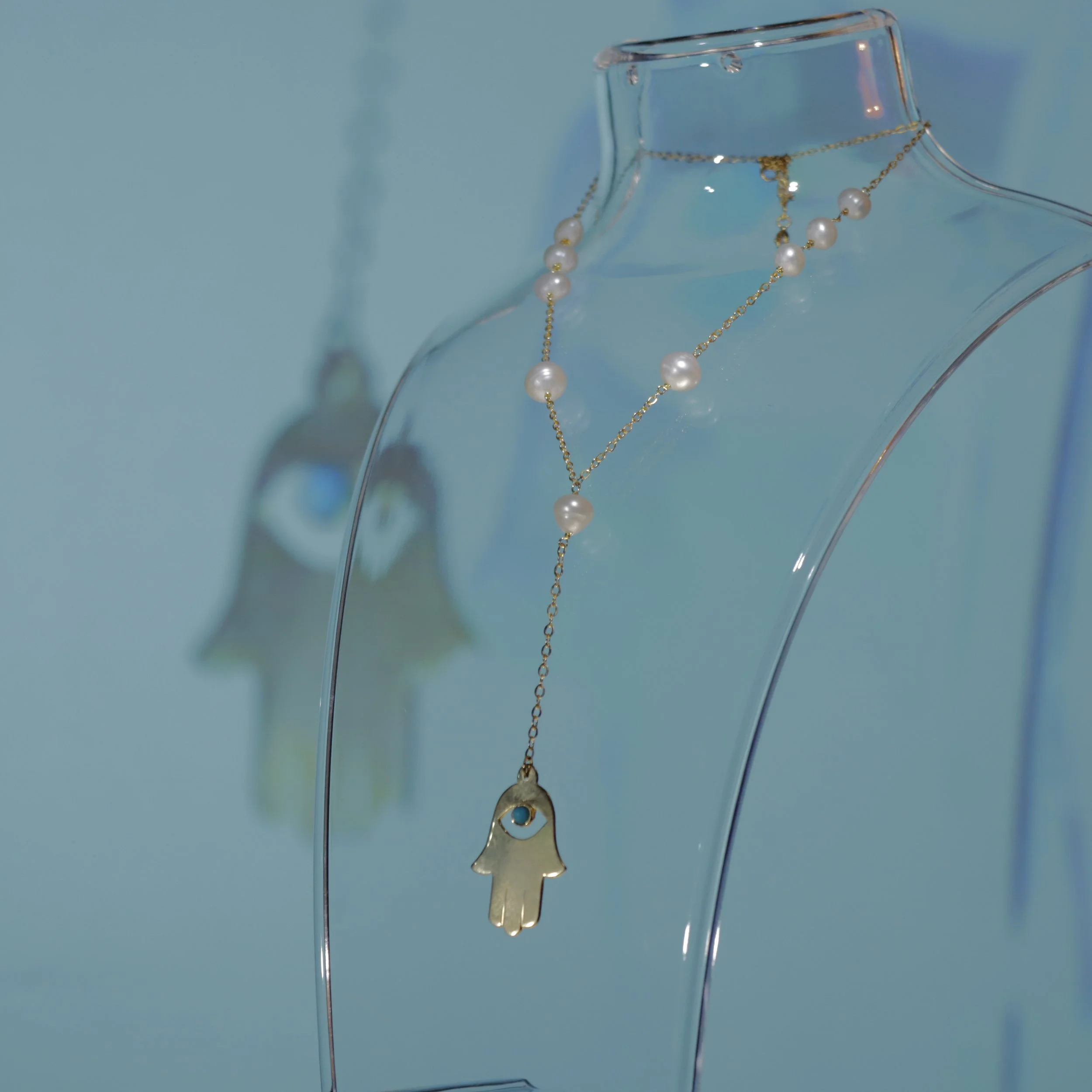 A necklace with white pearls and a gold chain draped over a clear glass mannequin bust, against a blue-green background.