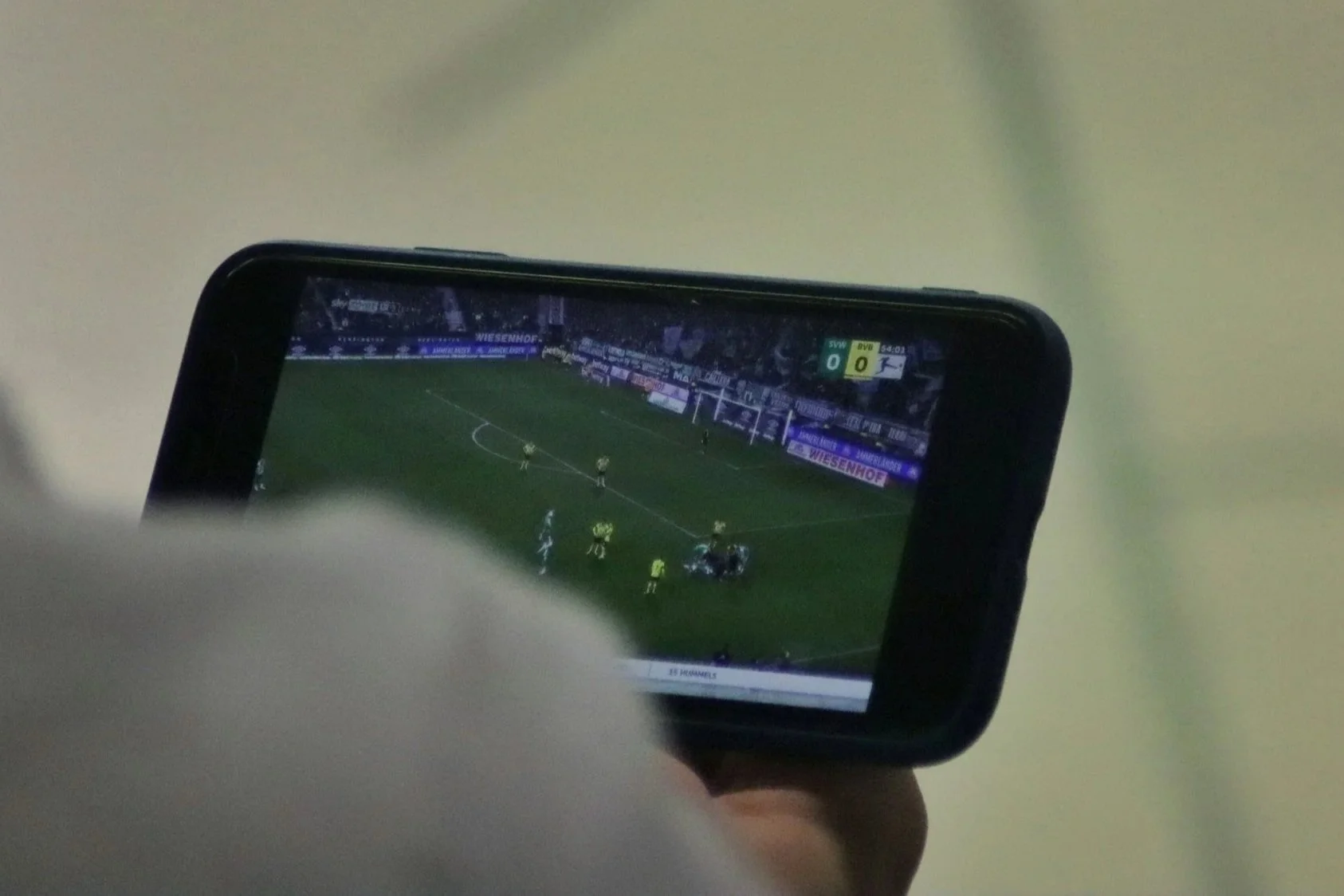 A person holding a smartphone showing a soccer match on the screen, with players and advertisements visible.