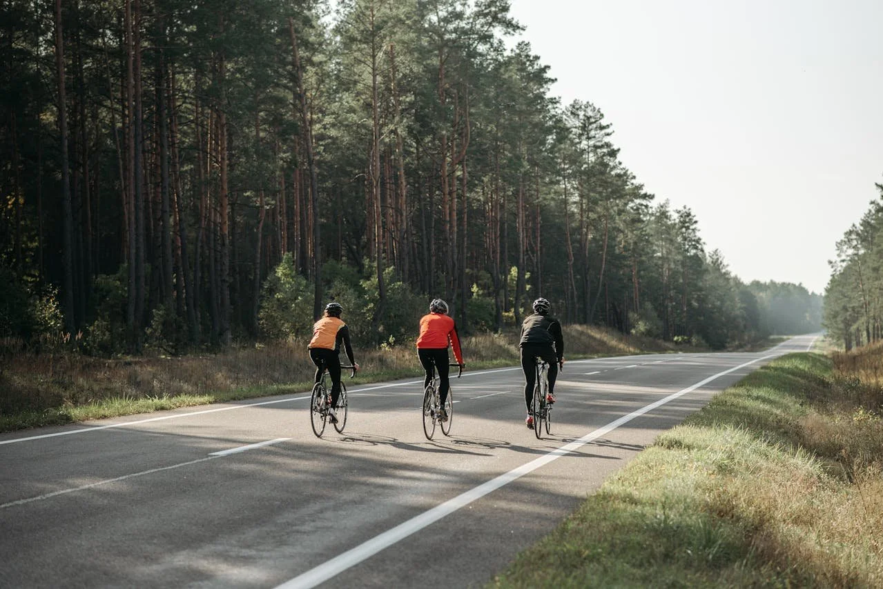 Three cyclists riding their bikes on a rural road surrounded by trees during daylight.