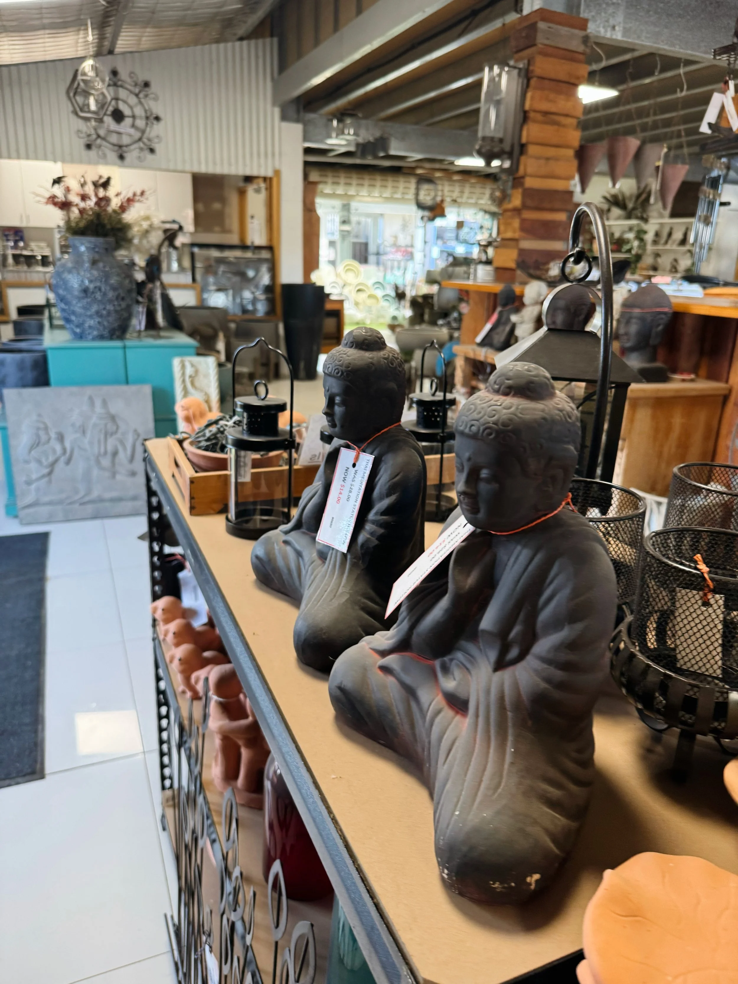 Display of various Buddha head sculptures on a store shelf with tags, alongside other decorative items in a retail shop.
