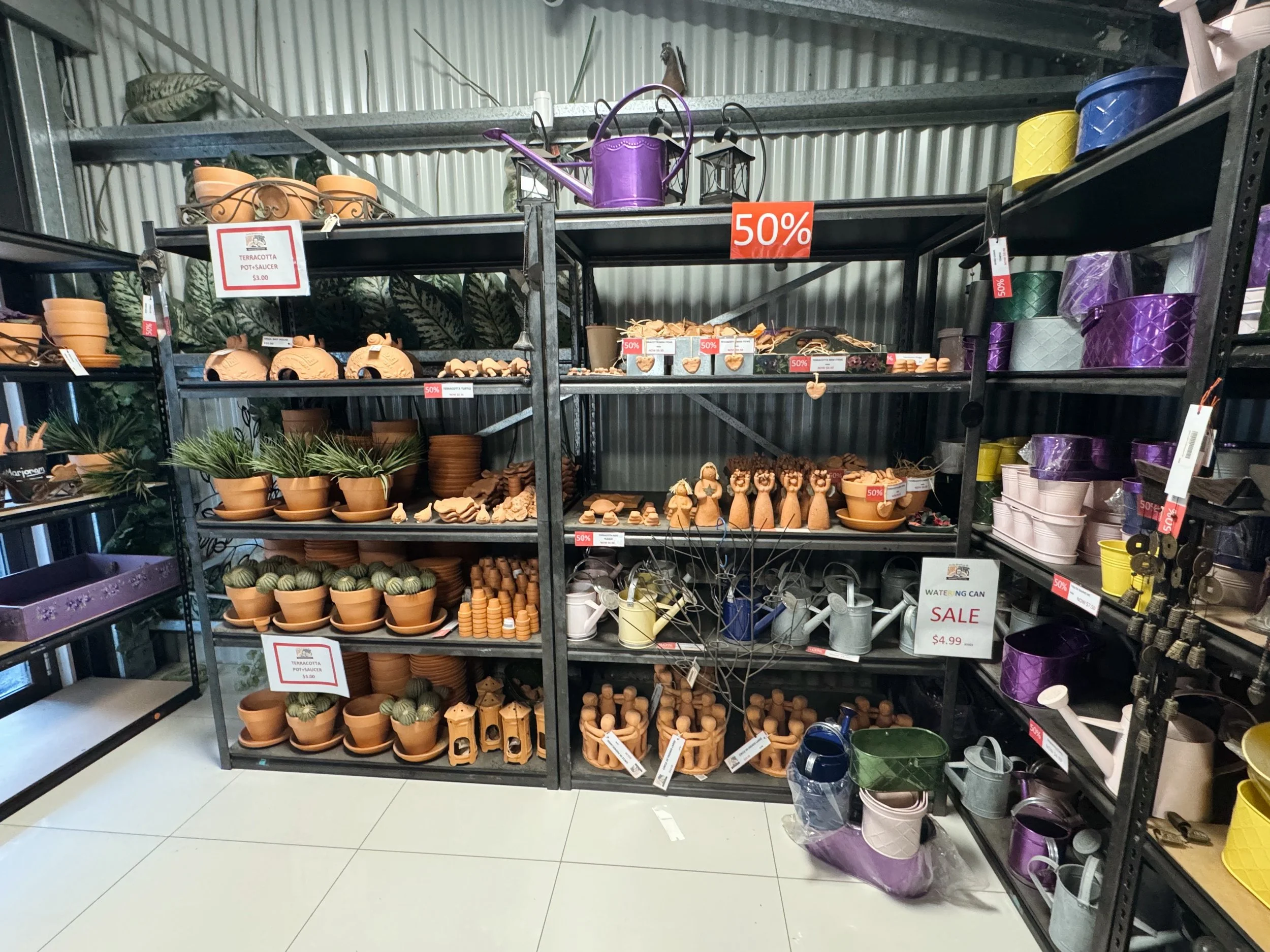 Store shelf filled with various terracotta gardening pots, planters, and outdoor decorations, with sale signs indicating discounts.
