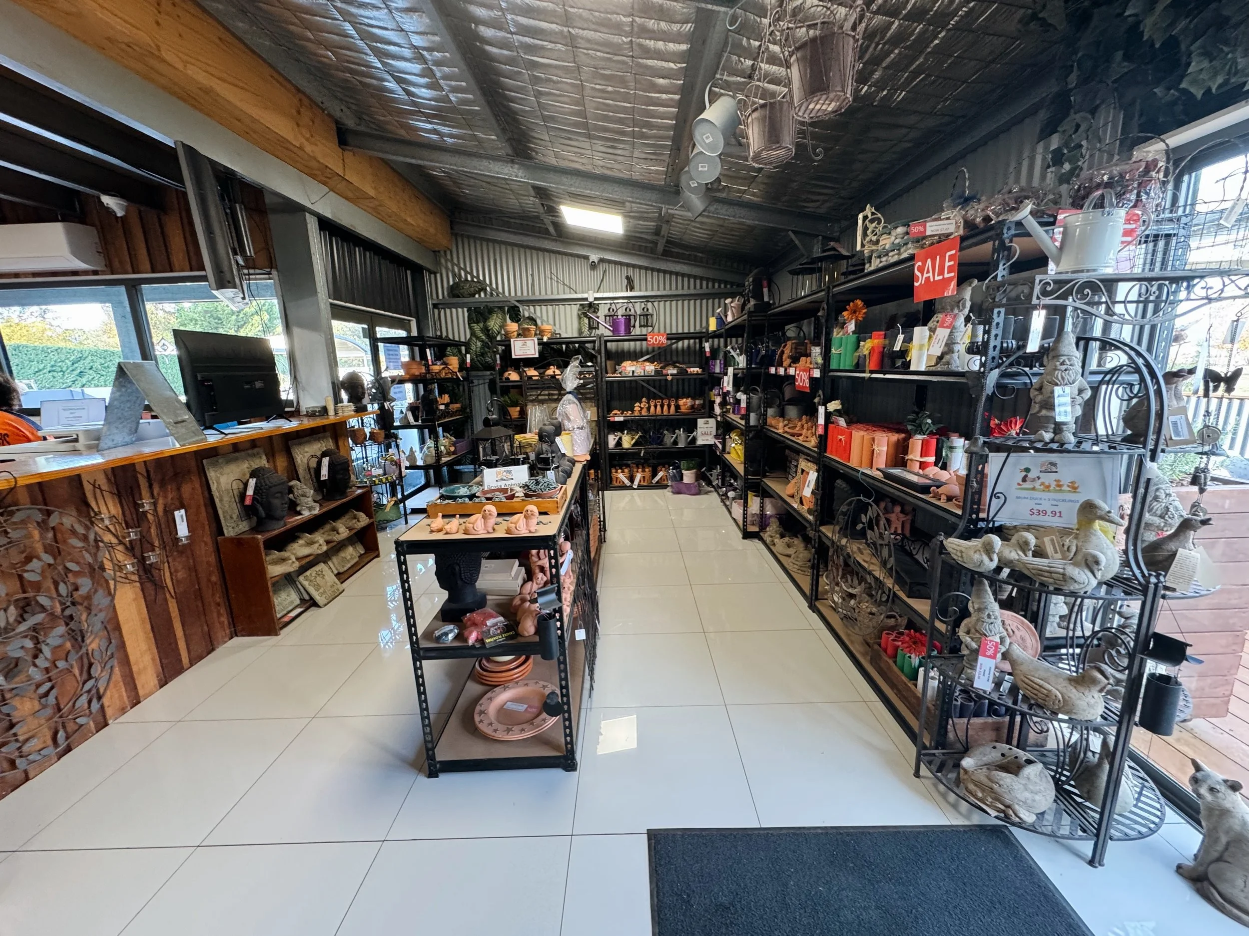 Interior of a gift and home decor store with shelves displaying various ornaments, figurines, and decorative items, sale signs indicating 50% off, and a front desk with a computer and framed pictures.