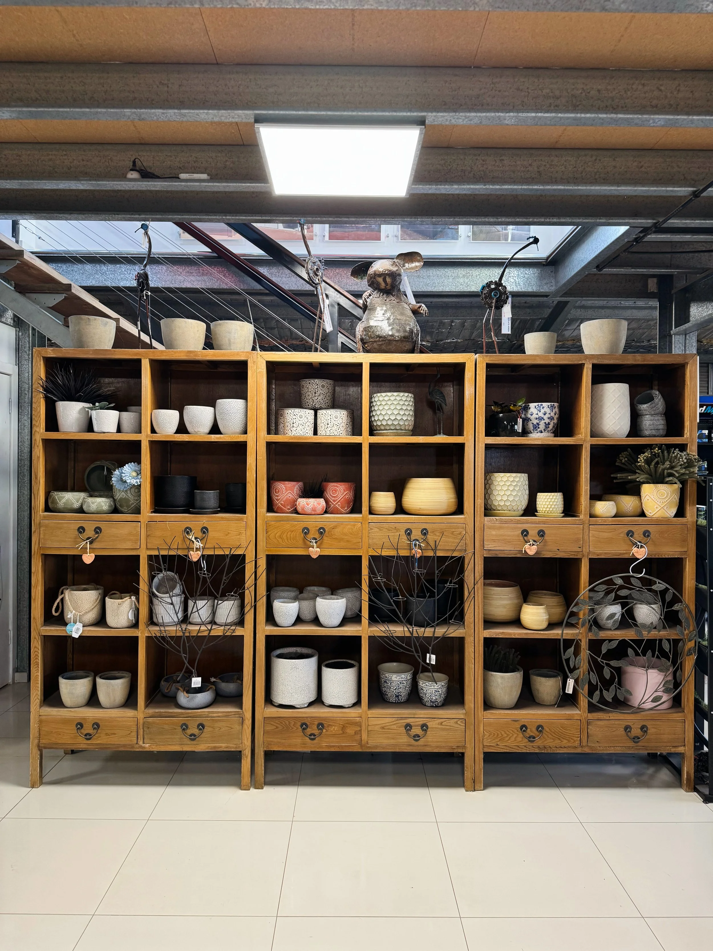 A wooden display shelf filled with various ceramic pots and vases, some with decorative patterns, in a store setting.
