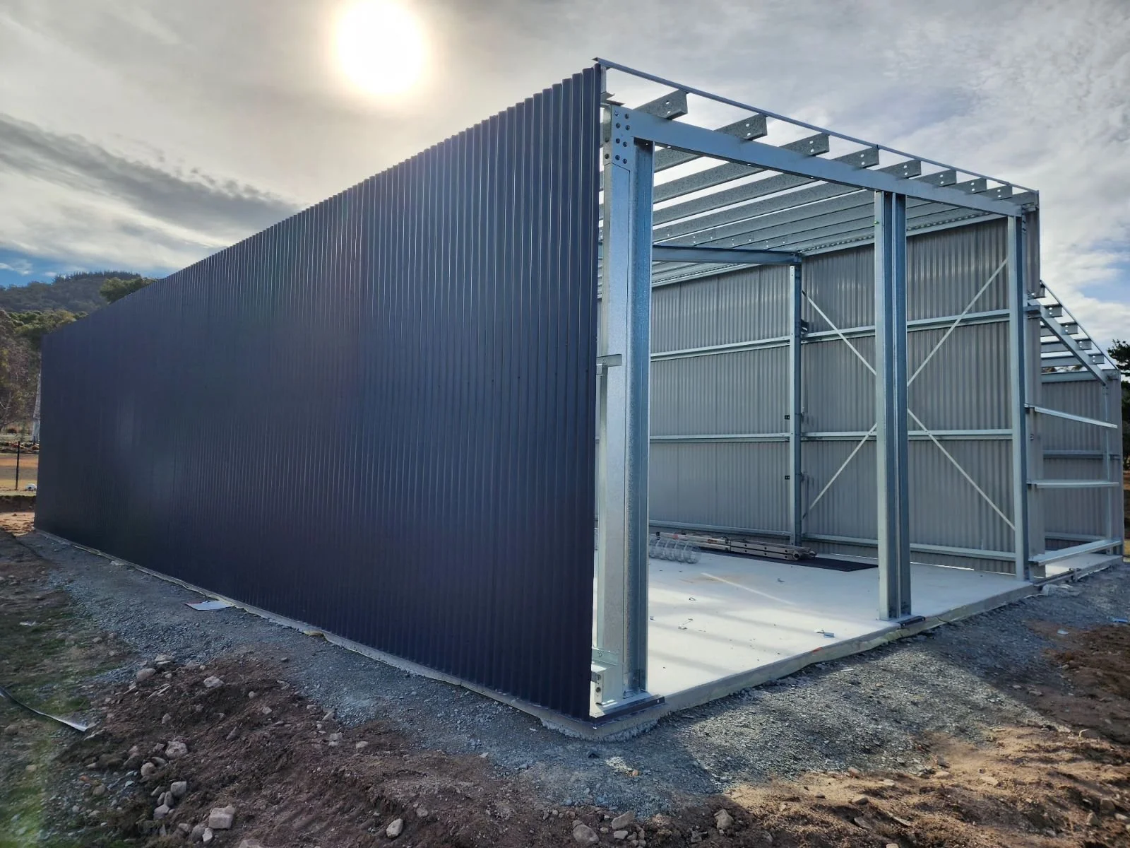 Steel frame structure of a building with corrugated metal walls under construction, outdoors on a partly cloudy day.