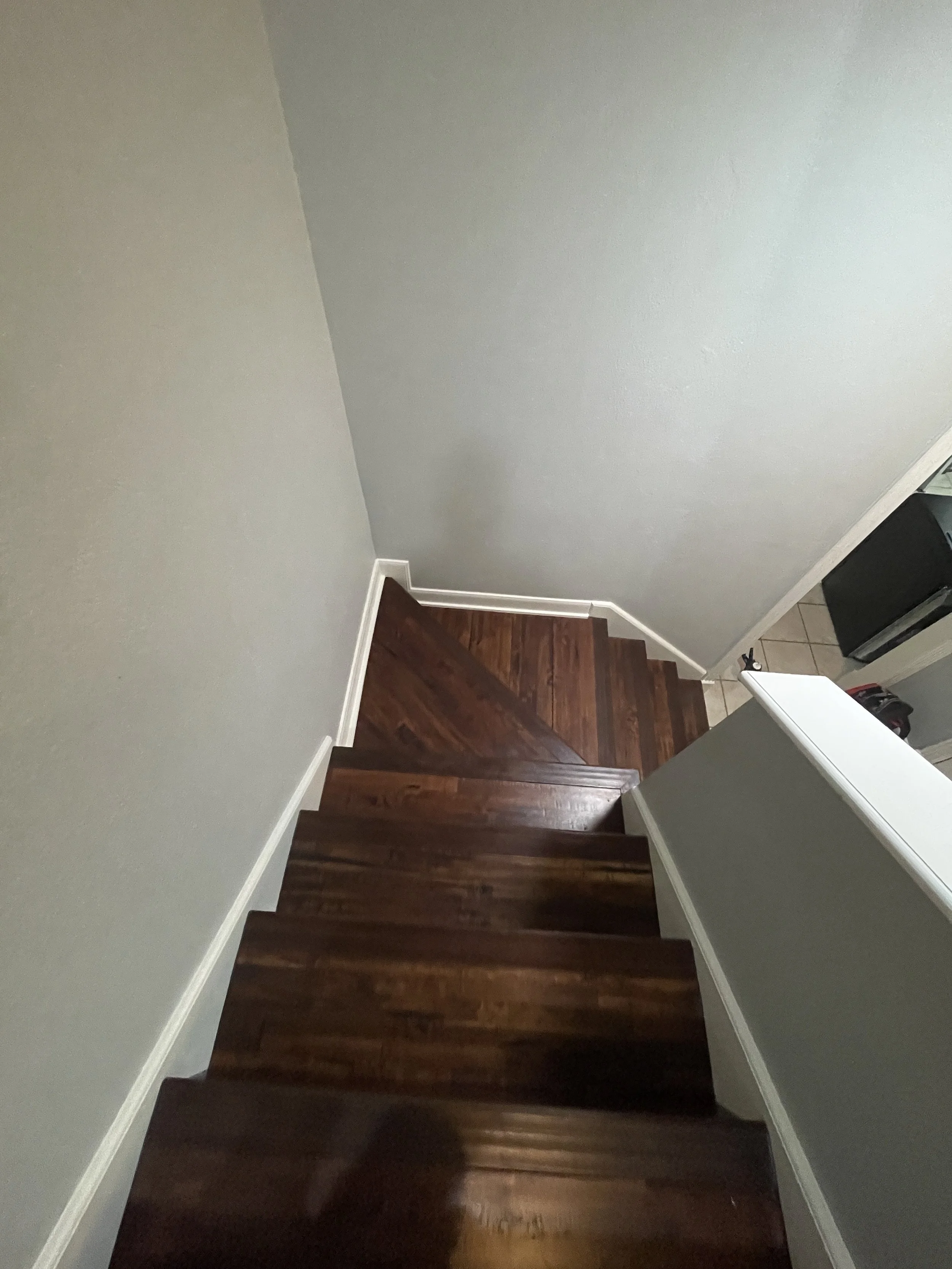 Interior view of a staircase with dark wooden steps and gray walls, leading from a tiled floor area to an upper level.
