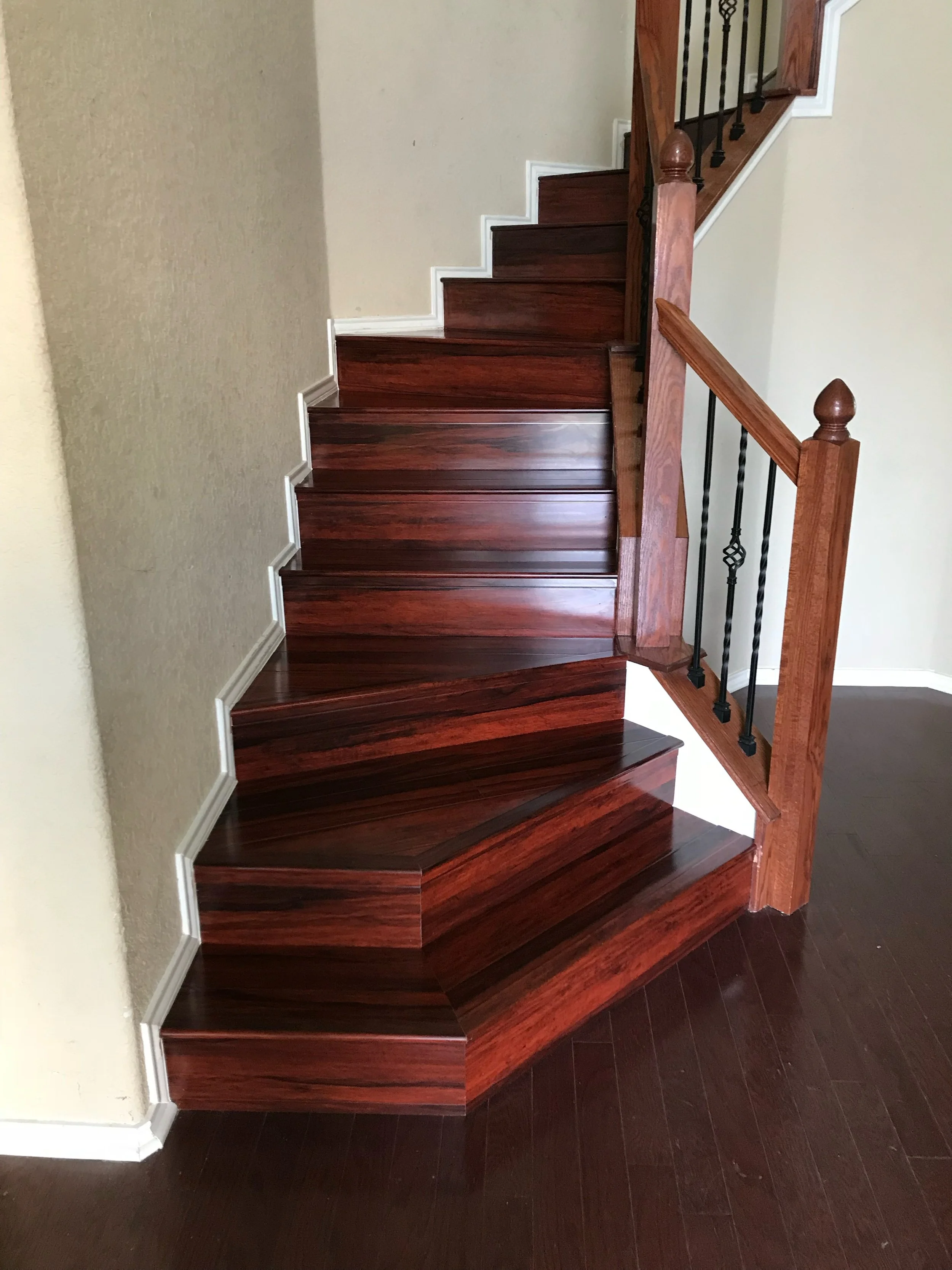 Wood staircase with dark wood steps, white risers, decorative black metal balusters, and a matching wooden handrail.