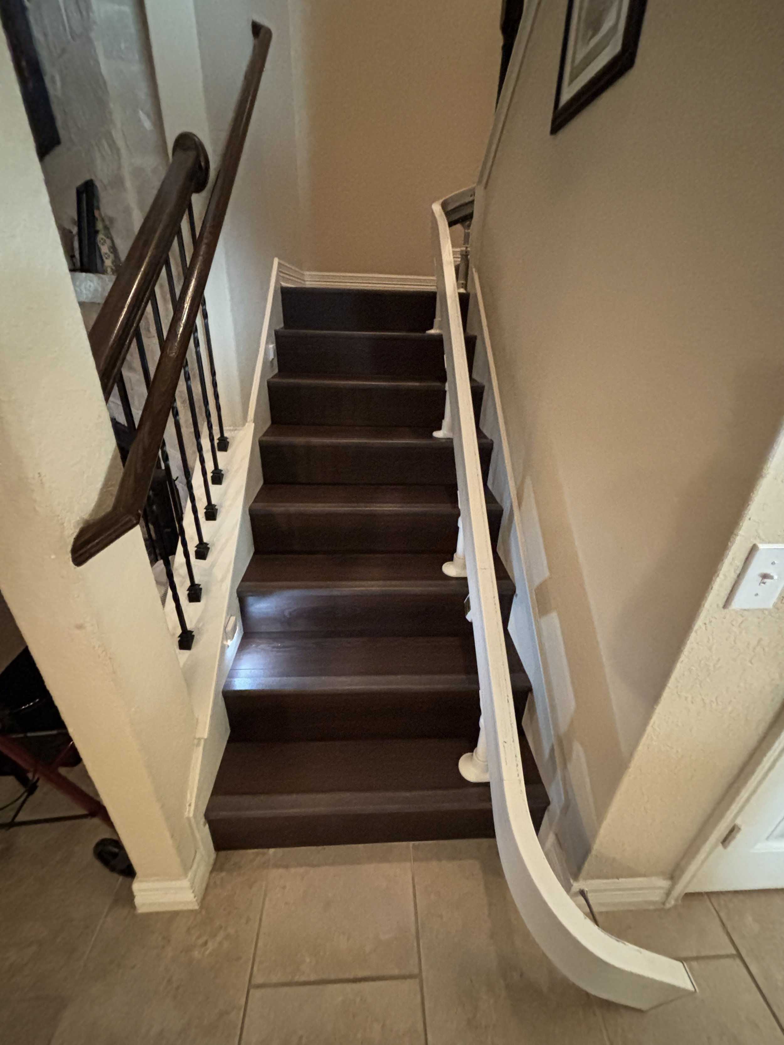 Indoor staircase with dark wooden steps, white railings, and beige walls, viewed from the bottom looking up.