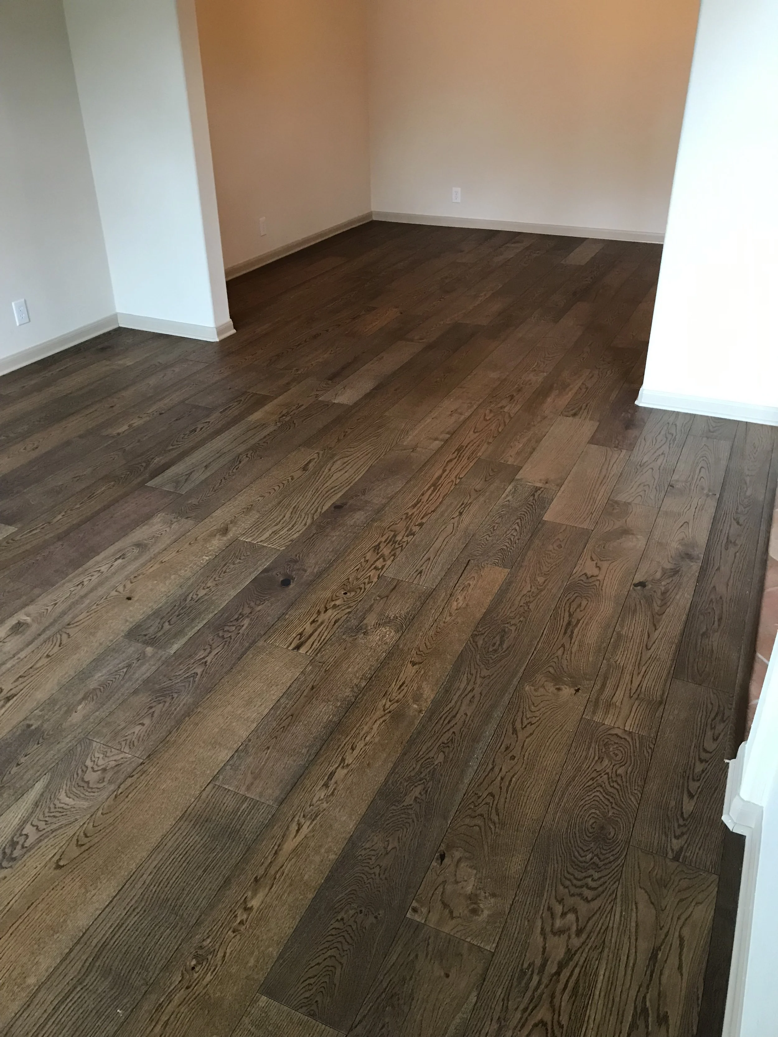 Empty room with hardwood flooring and beige walls, corner of the room visible.