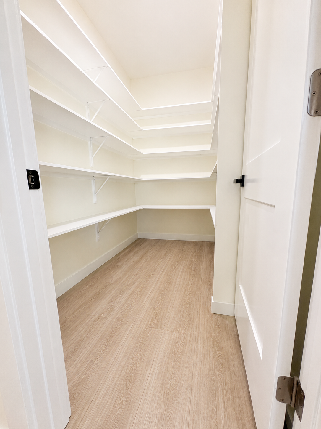 Empty walk-in pantry with white shelves and light wood flooring.