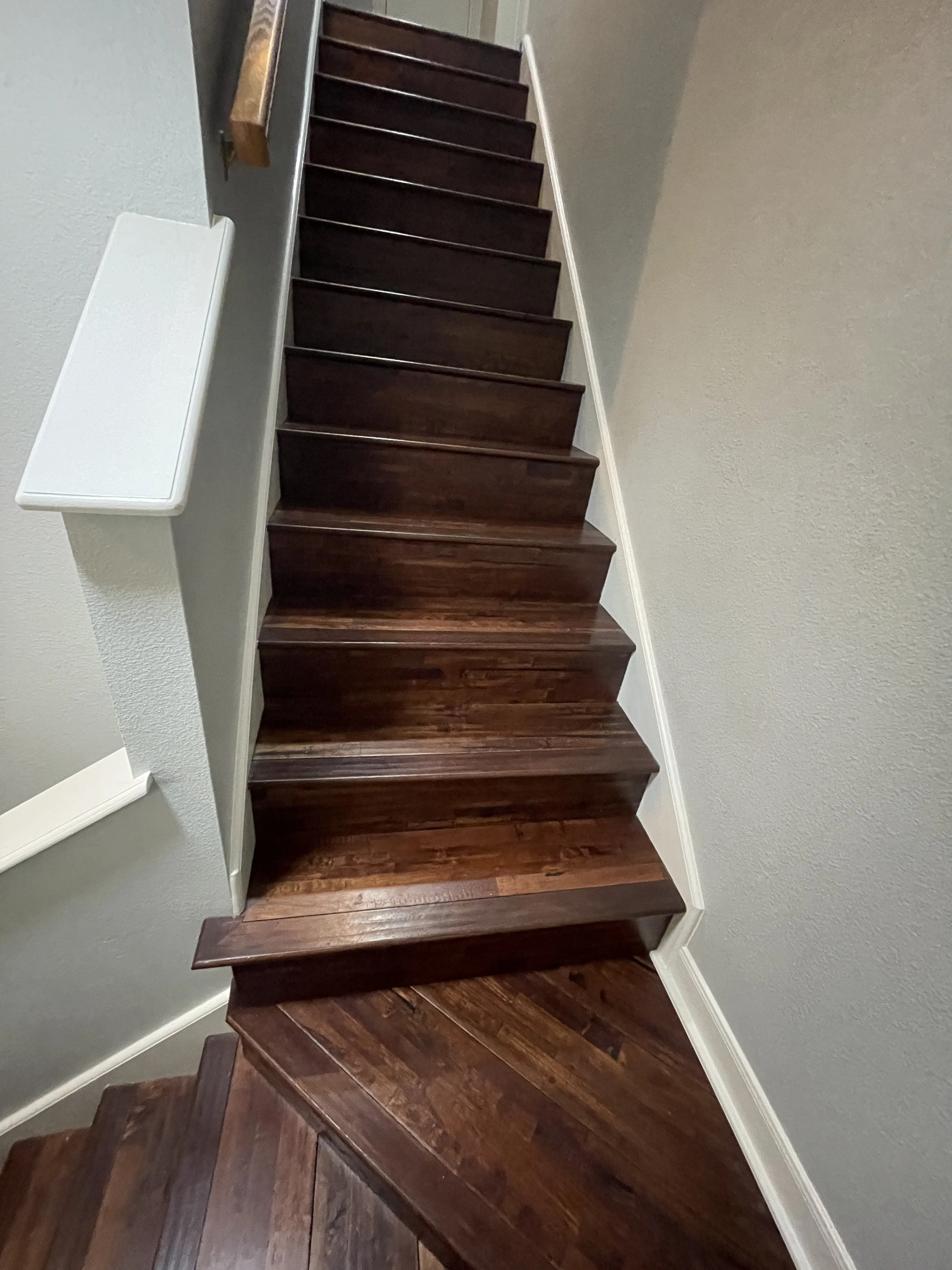Interior view of a staircase with dark wooden steps and beige walls, white baseboards, and a wooden handrail on the left side.