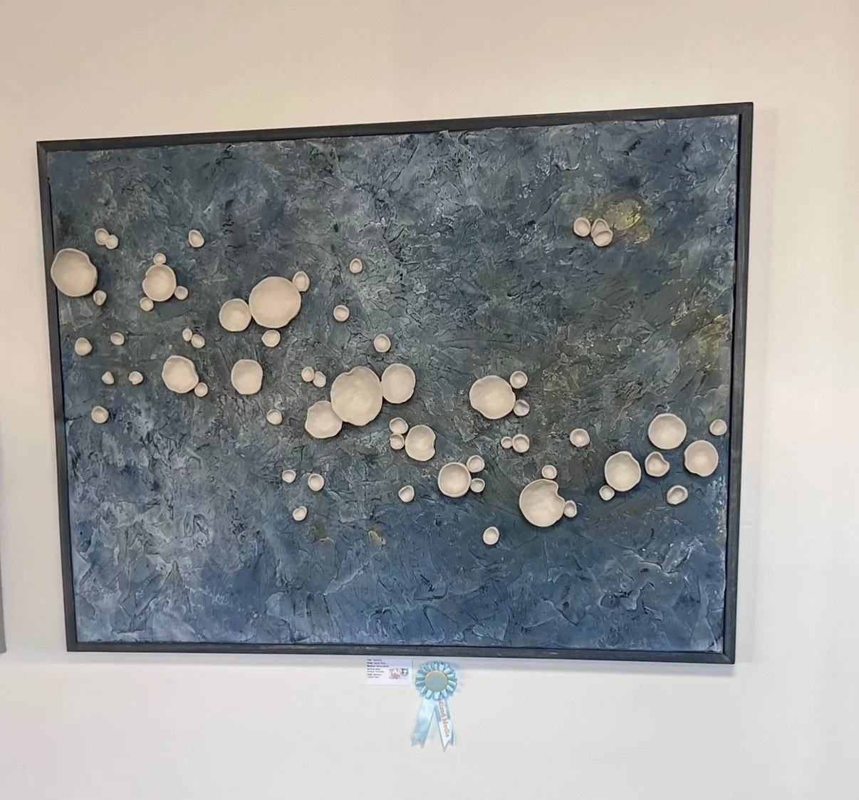 Abstract textured blue background with numerous white pottery-like spheres of various sizes attached, showcased as a piece of modern art.